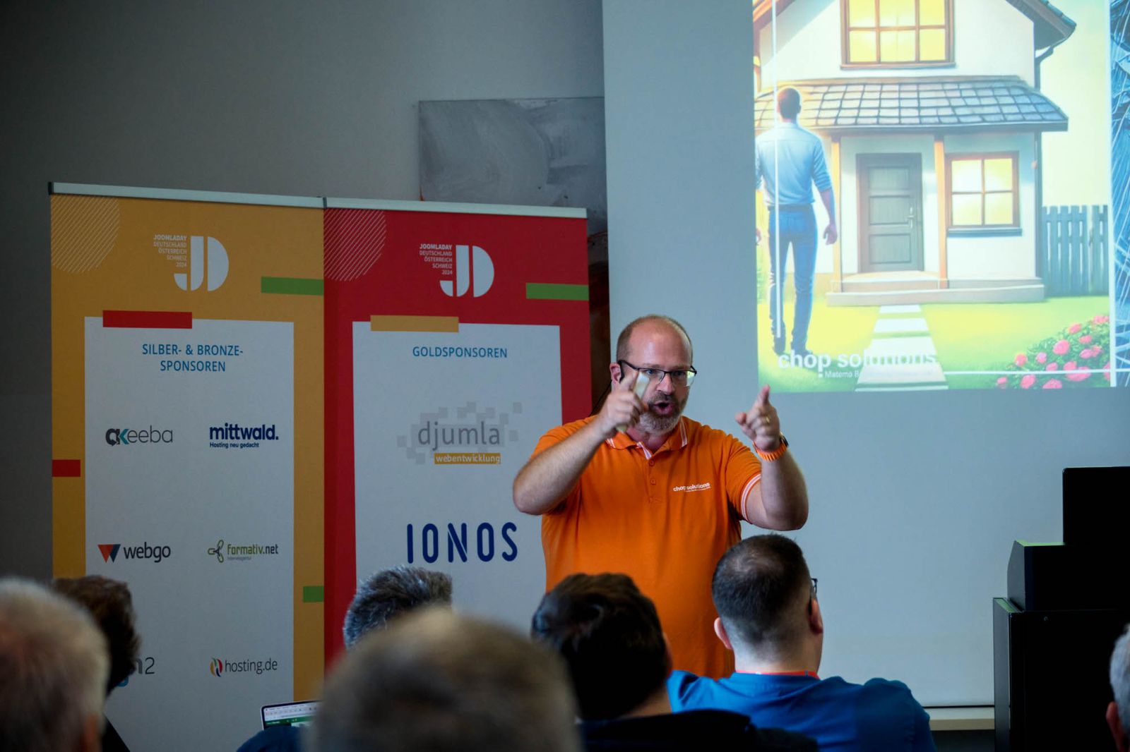 Joachim Nickel gestikuliert bei seinem Vortrag auf dem JoomlaDay 2024 vor den Sponsorenwänden