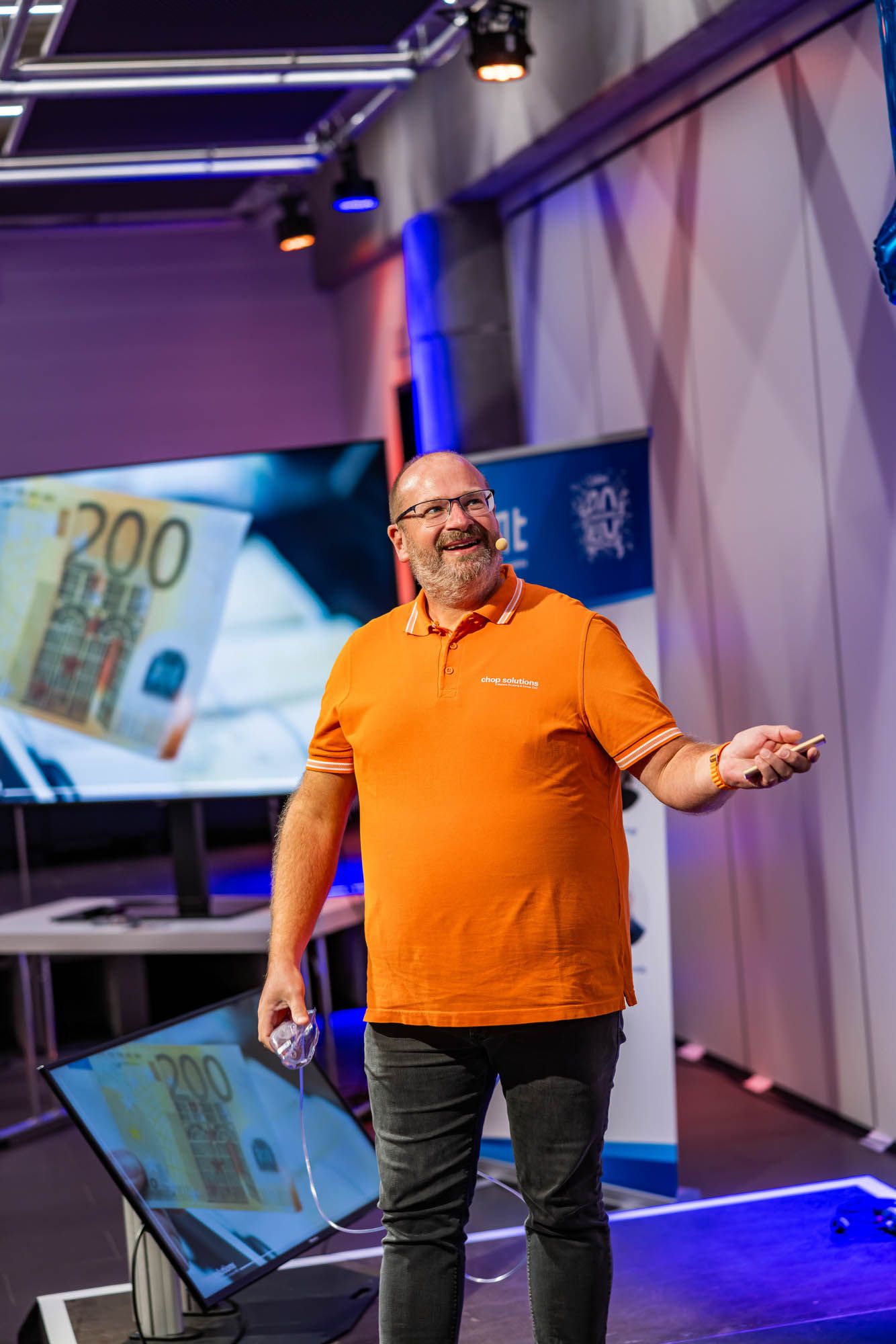 Joachim Nickel im orangen Polo-Shirt bei seinem Vortrag auf der OMT-Konferenz 2024 in Mainz