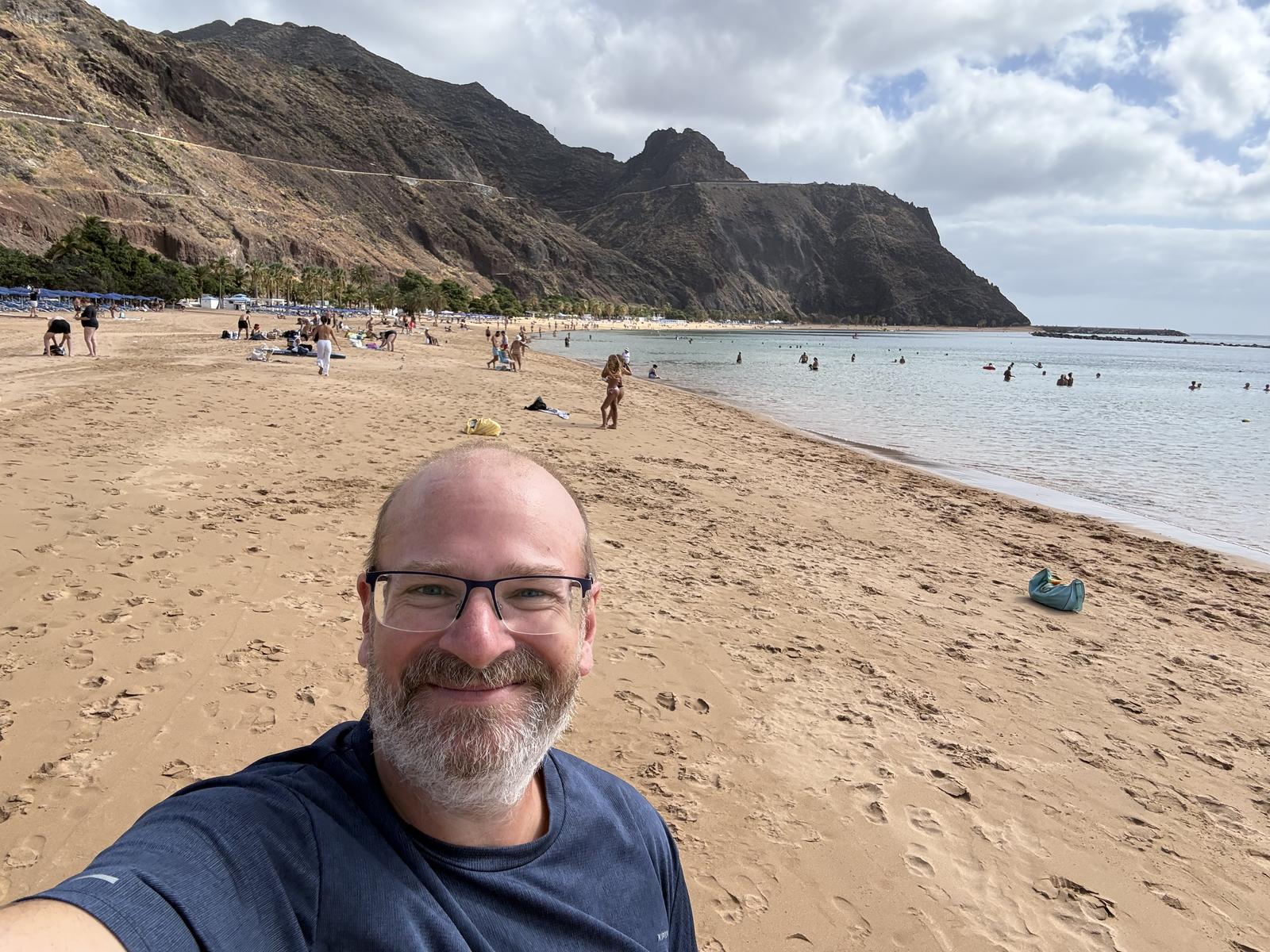 Joachim Nickel am Strand Playa de las Teresitas auf Teneriffa, im Hintergrund Berge und Meer